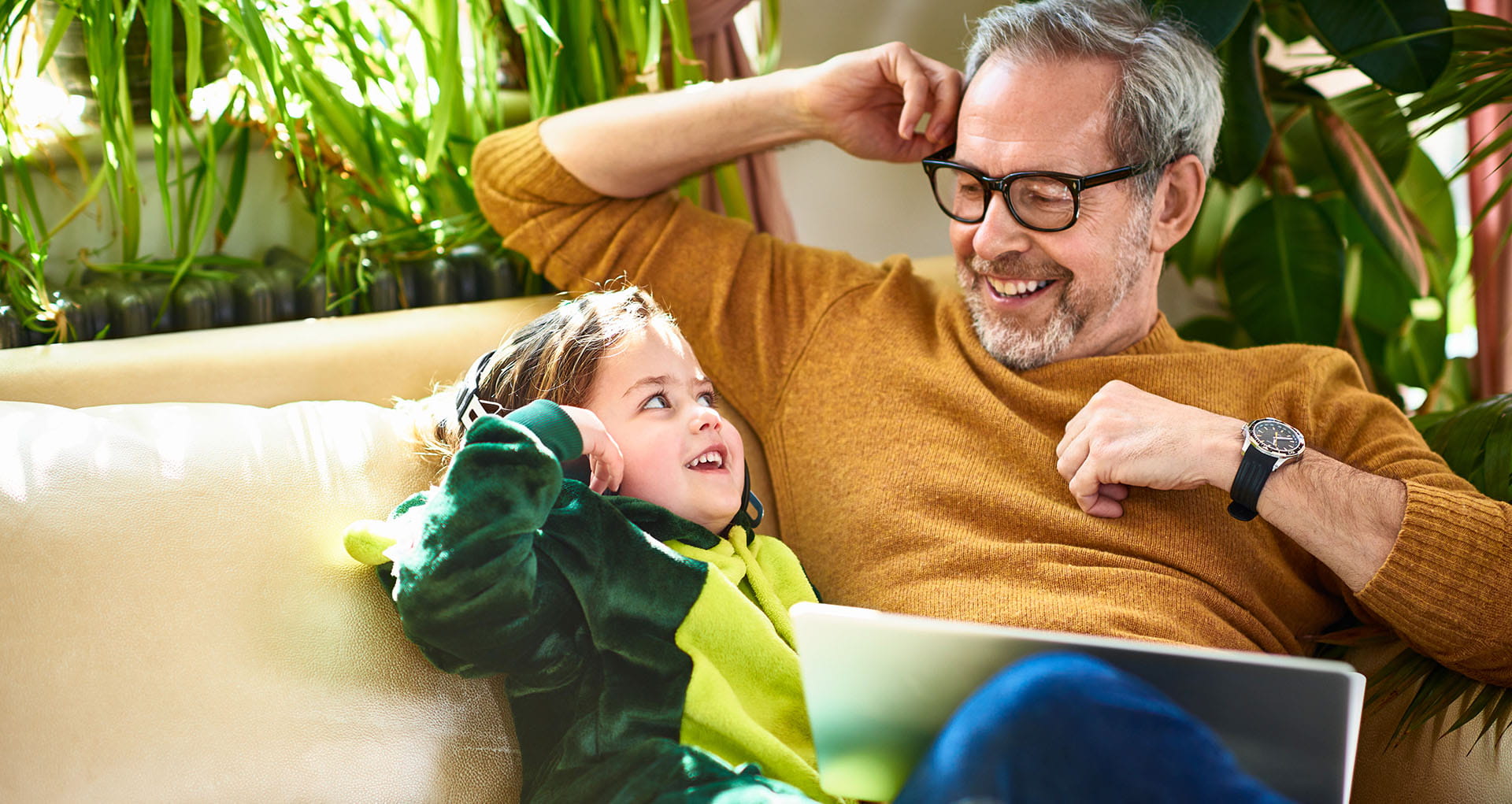 Man and child relaxing on a sofa and laughing together while watching something on their tablet.