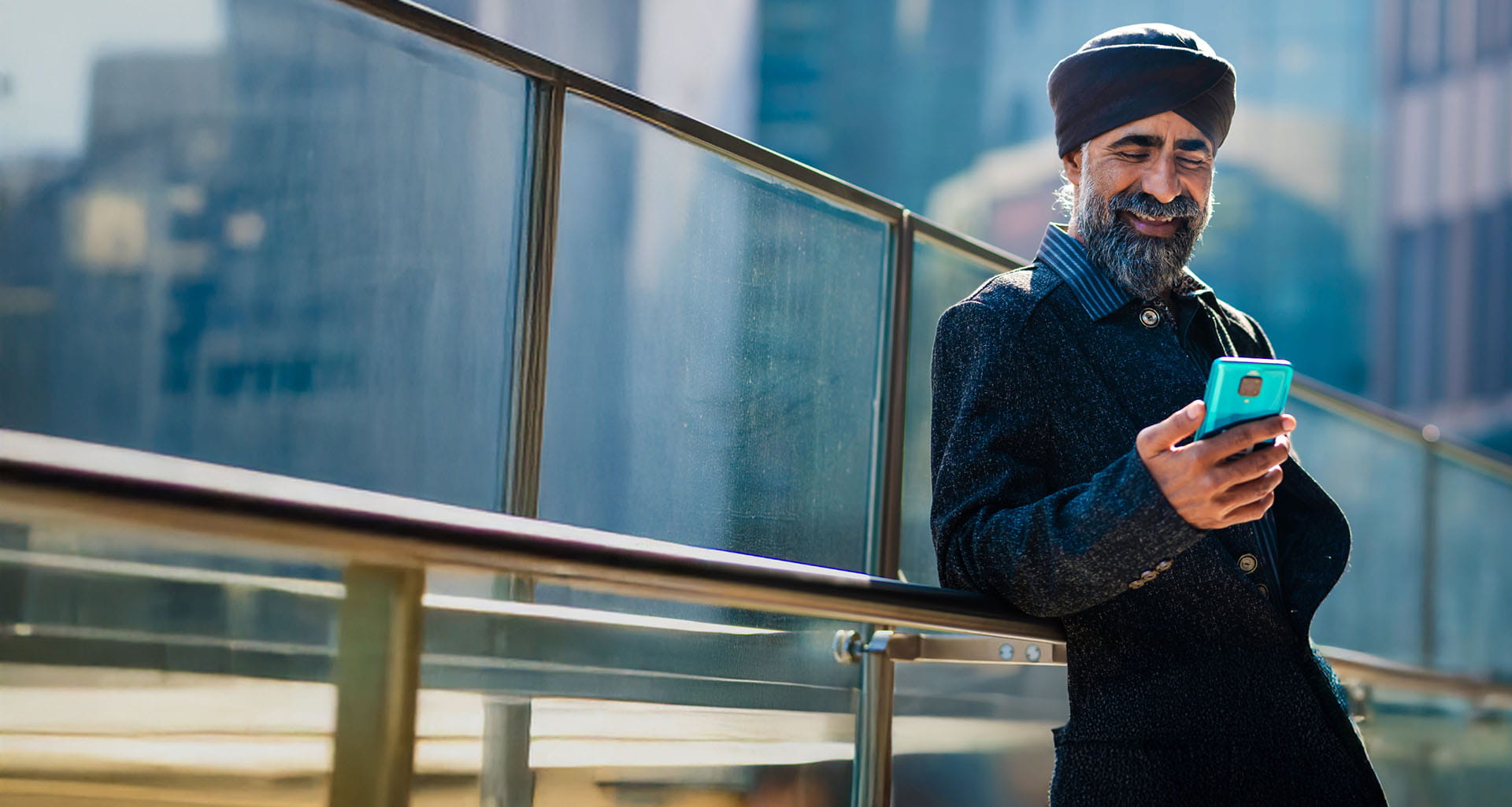 Man standing relaxed outside in a city environment and smiling while using his mobile phone.