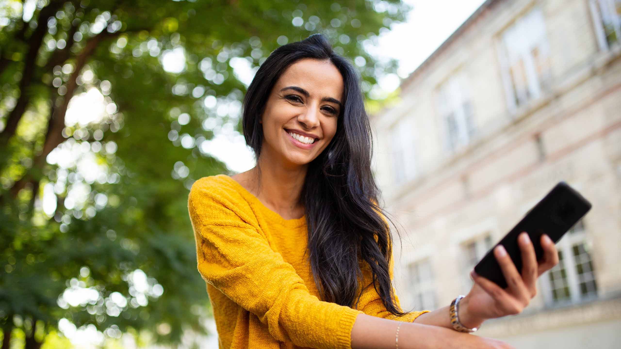 lady outside smiling with a mobile phone in her hand