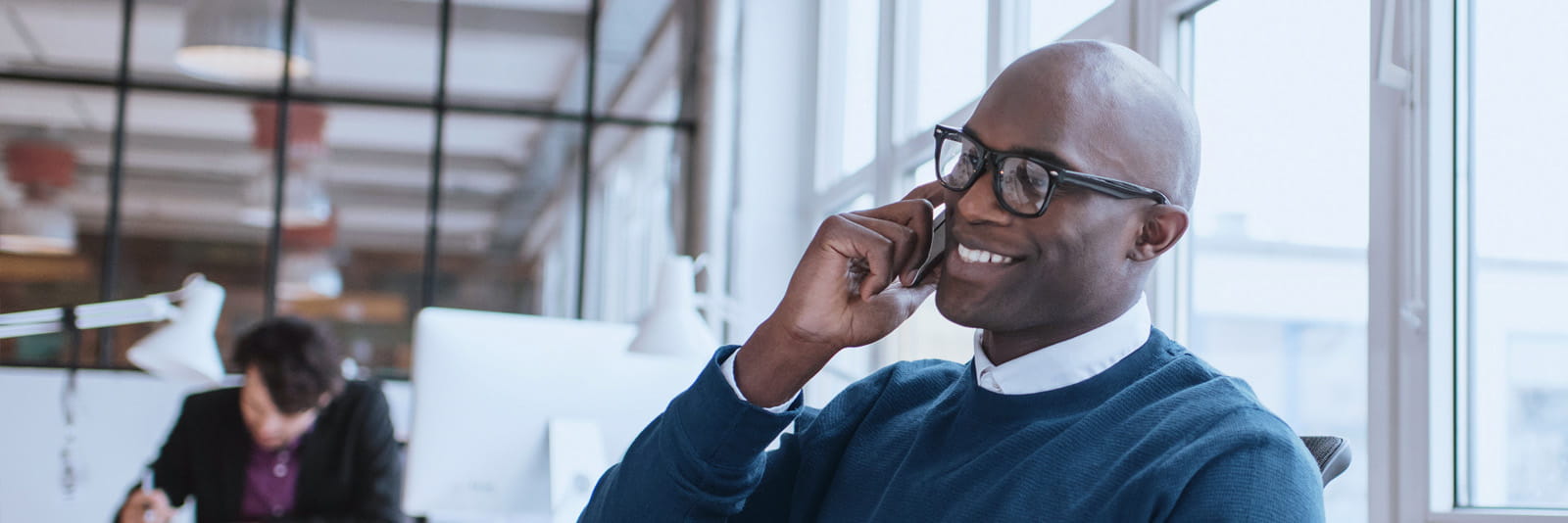 Office worker using mobile phone at desk with laptop and papers