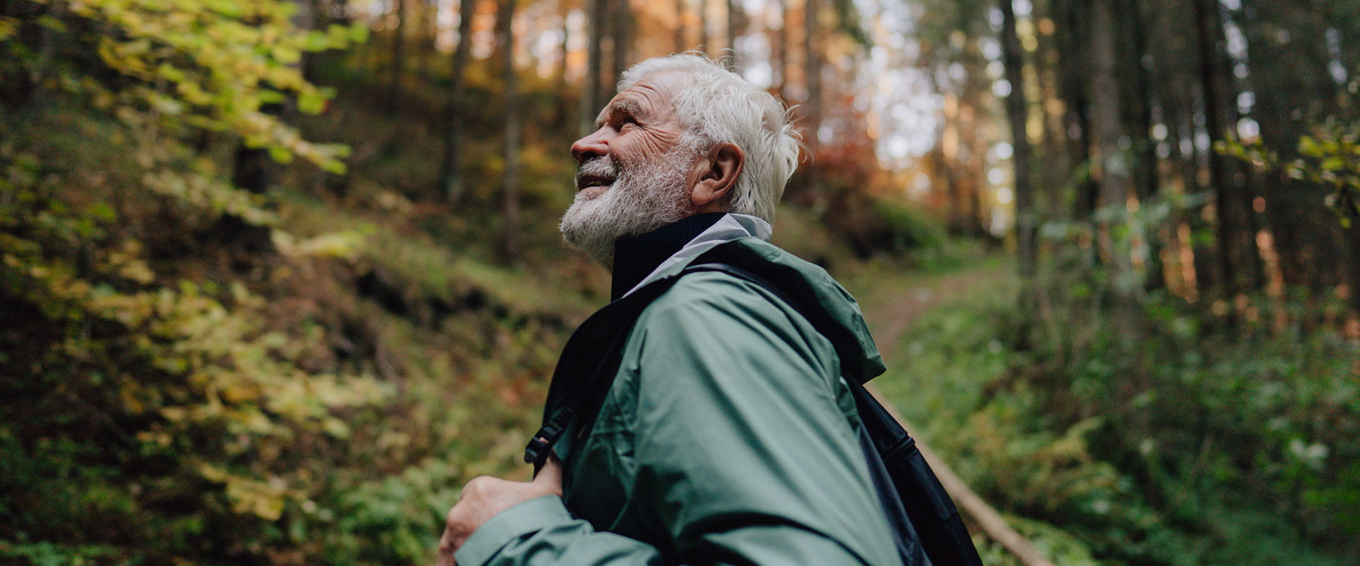 Gentleman hiker wearing a waterproof coat while walking through an autumnal forest.