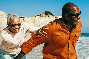 Man and woman holding onto each other, happy in each others company on a sunny, windswept beach.