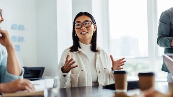 Person speaking to colleagues during meeting with coffees on table