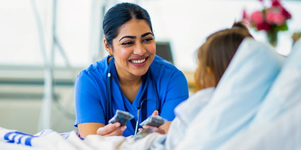 Medical professional sitting at the bedside of a patient in hospital and smiling while talking to each other.