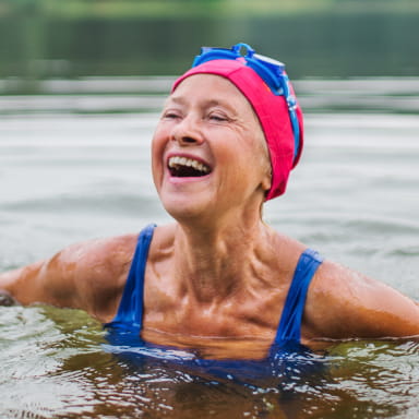 Woman in swimsuit and swimming hat enjoying a cold water swim in a lake on a brisk day.
