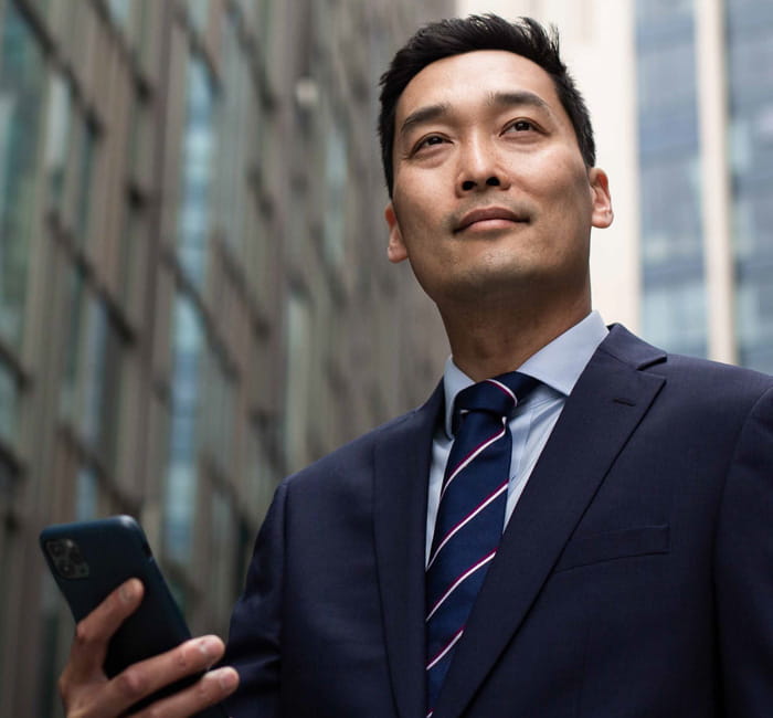 Man in business suit holding a mobile phone while on the street