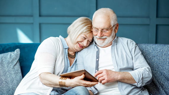 elderly couple happily looking at tablet on a sofa