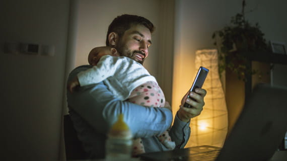 New dad comforting baby while checking mobile phone