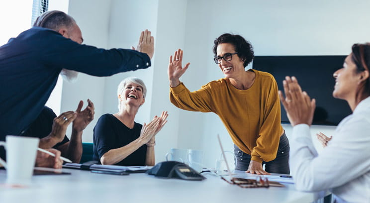 Group of employees around office table smiling and clapping