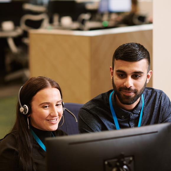 Two customer service advisors working together at a computer in an office