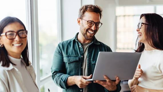 Three colleagues standing and laughing around a laptop