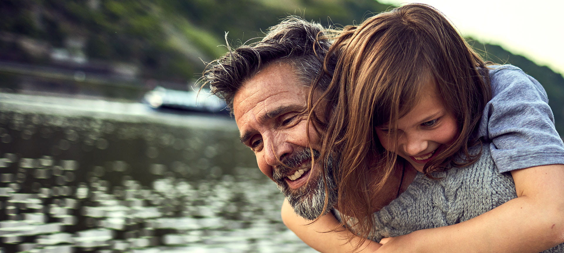 Man carrying his daughter on his back near a river