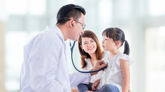 doctor examining a girl with stethoscope, with mother smiling in the background