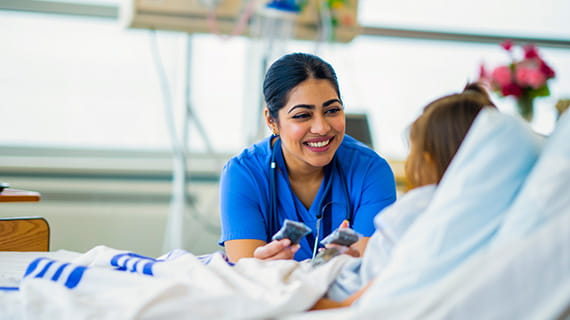 Female medical professional talking to a child patient who is lying in a hospital bed