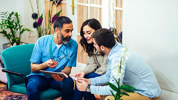 Male medical professional talking to a couple, the woman is smiling at what she sees on a tablet screen