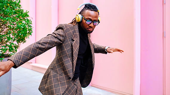 Man in a suit wearing headphones and glasses, dancing in the street