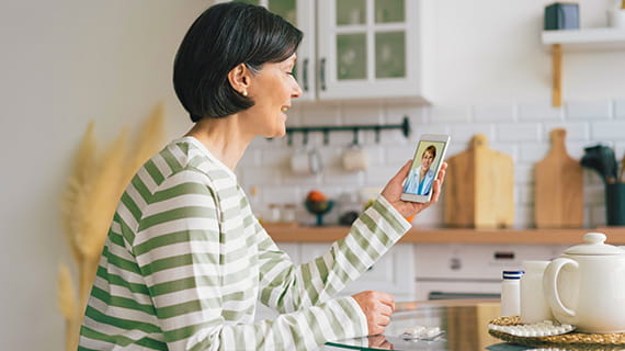Woman wearing green and white striped clothes, sitting in a kitchen taking a video call