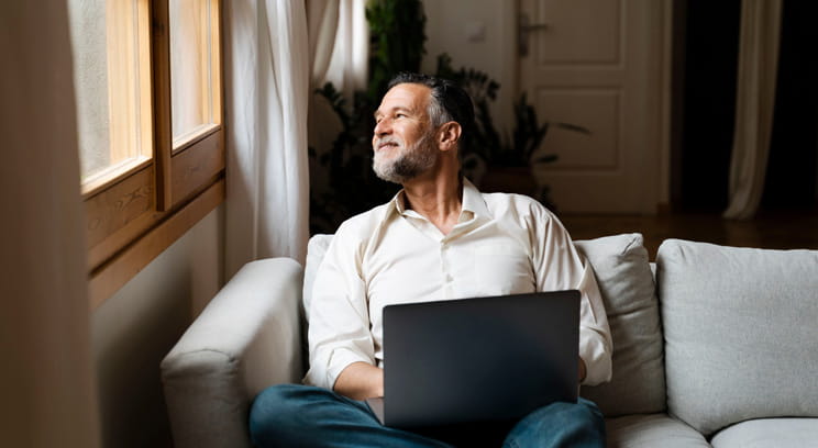 Man sitting in a relaxed position on his sofa at home, with a laptop on his lap.