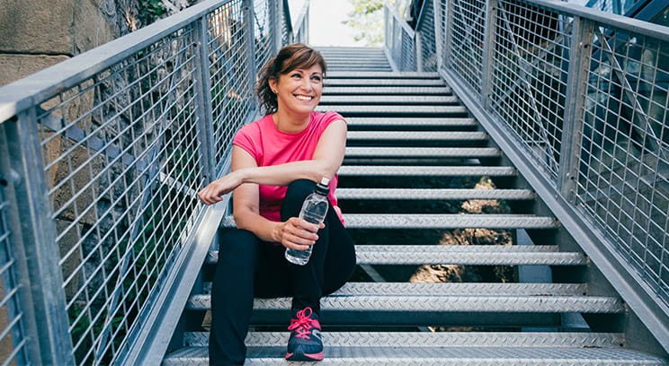 Woman in exercise clothes, sitting on steps with a bottle of water, taking a rest after a workout