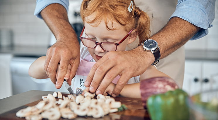 Young girl having a cooking lesson with a relative and being helped to chop vegetables