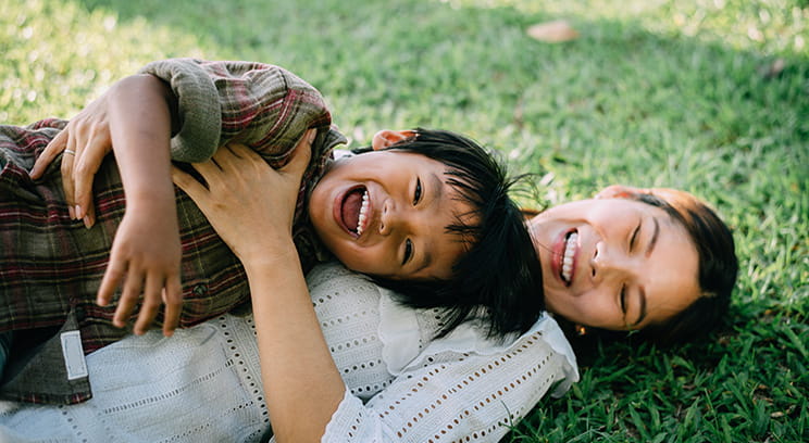 Child and mother laying on grass, playing and smiling