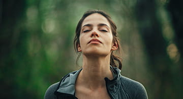 Young woman standing surrounded by trees in a forest, at peace with her eyes closed 