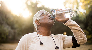 Man of colour with grey hair and beard takes a swig from his water bottle