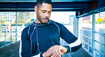 Young black male jogger stops to check his wearable wrist tech