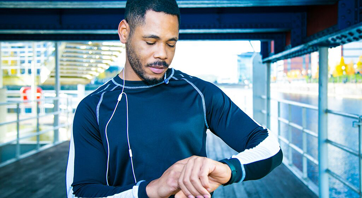 Young black male jogger stops to check his wearable wrist tech