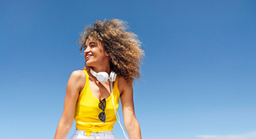 Young woman of colour wearing yellow top smiling against blue sky