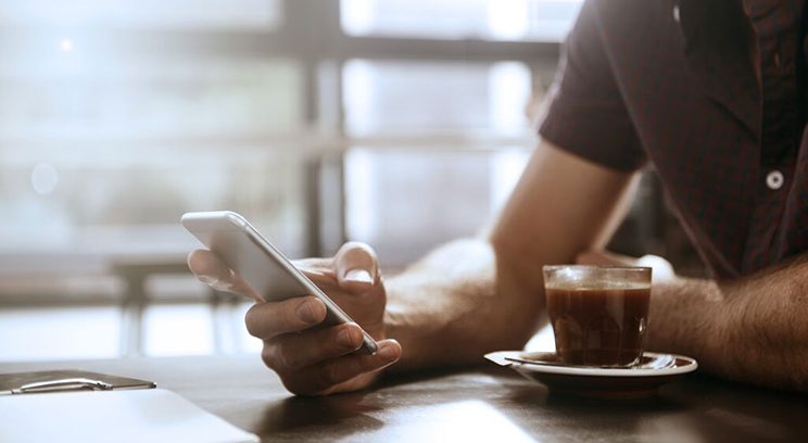 Man sits at table using mobile phone with coffee