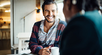 Smiling man sits at table drinking coffee with friend