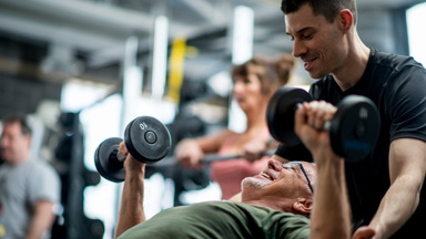 personal trainer helping an older man with a dumbbell bench press