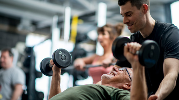 Personal trainer helping an older man with a dumbbell bench press
