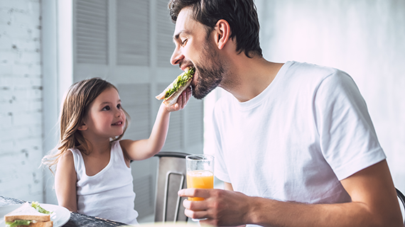 Child feeding her father a sandwich making informed healthy dietary choices.