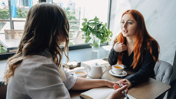 woman opening up to a friend at a small table with coffee and tea