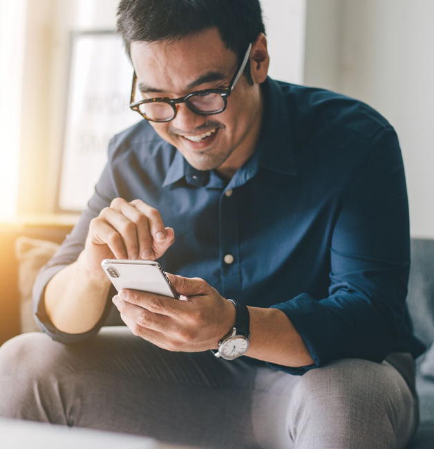 Man sitting on sofa at home and happily looking down at smartphone