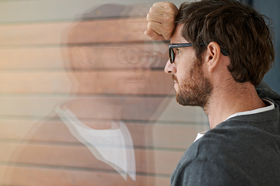 Thoughtful young man leaning against a glass window in his office