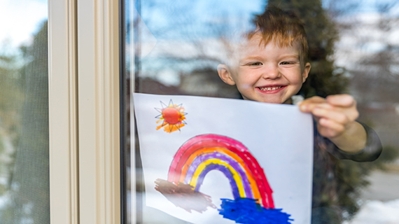 young boy holding rainbow picture in window