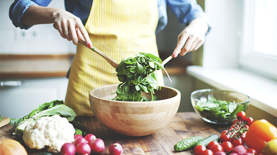 woman tossing salad in wooden bowl