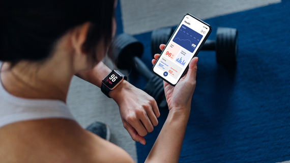 person in gym holding a mobile phone with health information in app and comparing to smart watch