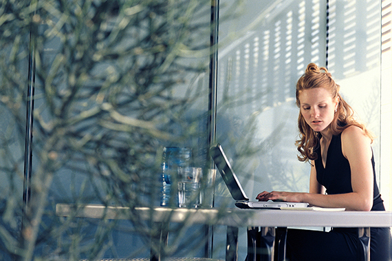 woman with red hair sitting at desk working on laptop and reviewing notes