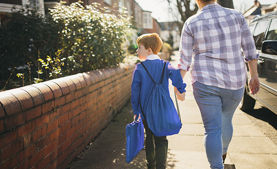 parent walking down residential street with child in school uniform