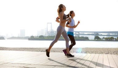 two women running along a beach with the city in the background