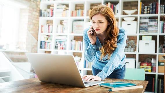 A female senior executive working from home in an office on a laptop while taking a phone call