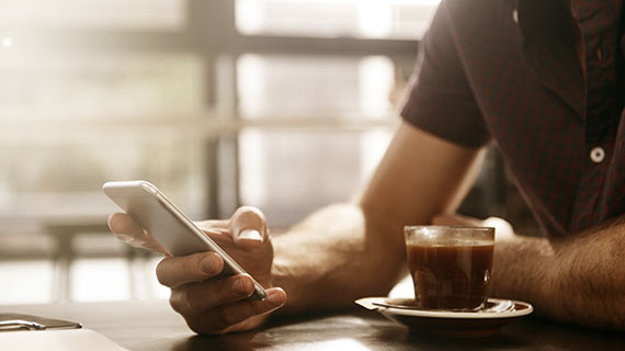 man holding a mobile phone sat next to a coffee