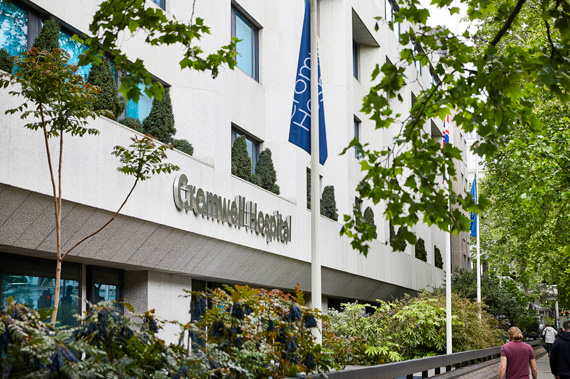 Exterior of the Cromwell Hospital with blue flags in front of the building and people walking along the street