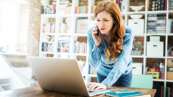 woman working on a laptop and on a call on a mobile phone simultaneously in office