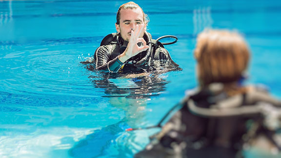 A scuba diving instructor teaching the OK sign to a beginner diver