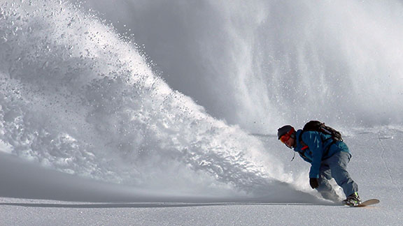 Man snowboarding kicking up snow powder behind him